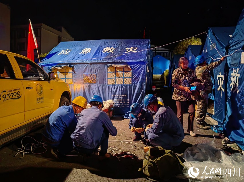 9月5日24時，國網眉山供電公司應急搶險隊員在瀘定縣磨西鎮用應急照明燈點亮磨西鎮公安分局群眾安置點后，馬不停蹄為安置點帳篷通電。王鴻飛攝